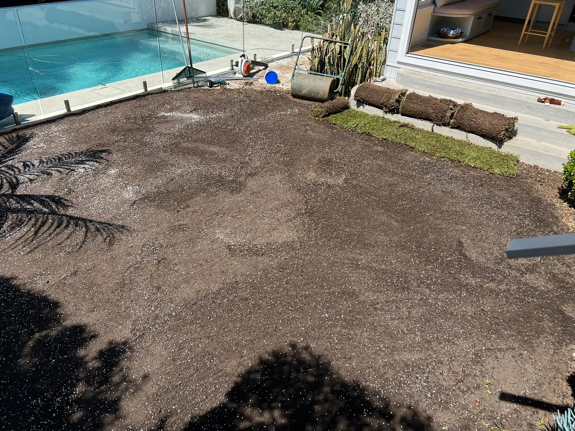 Prepared soil and turf rolls beside the glass pool fence in Balgowlah